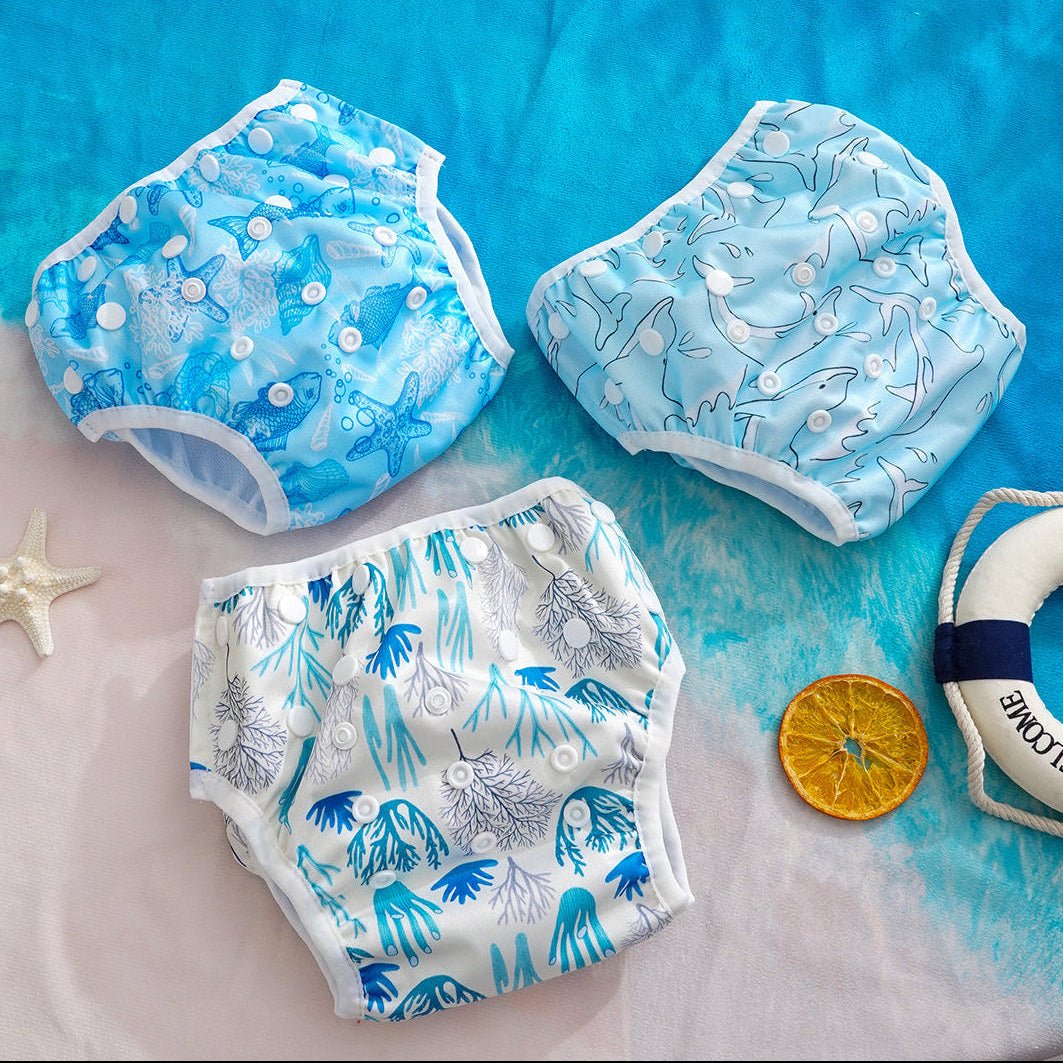 Three baby swim diapers with ocean-themed patterns on a blue and white textured surface.